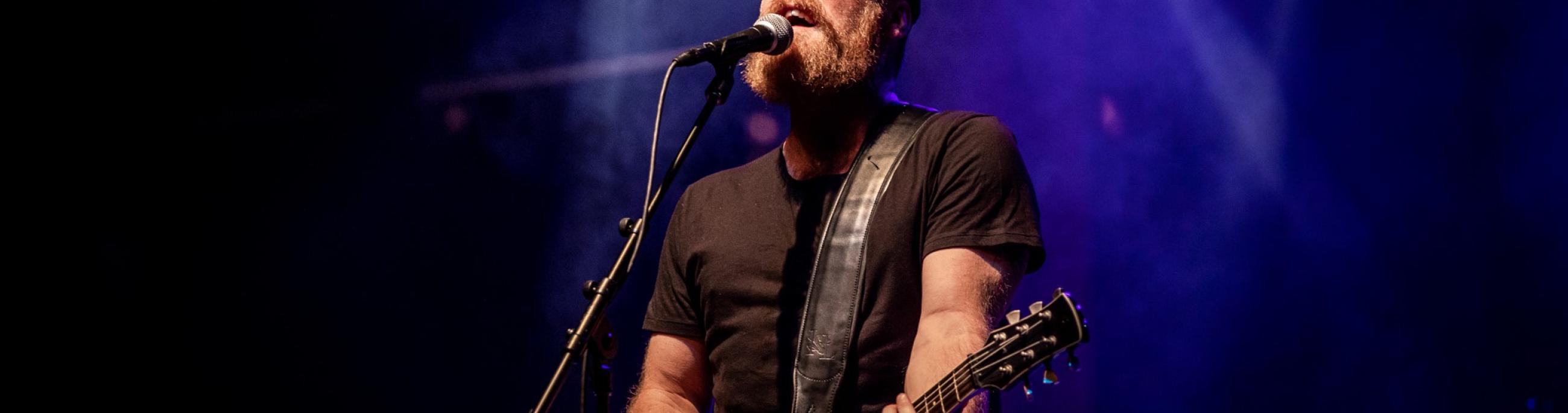 man with a beard in the spotlight singing into a microphone