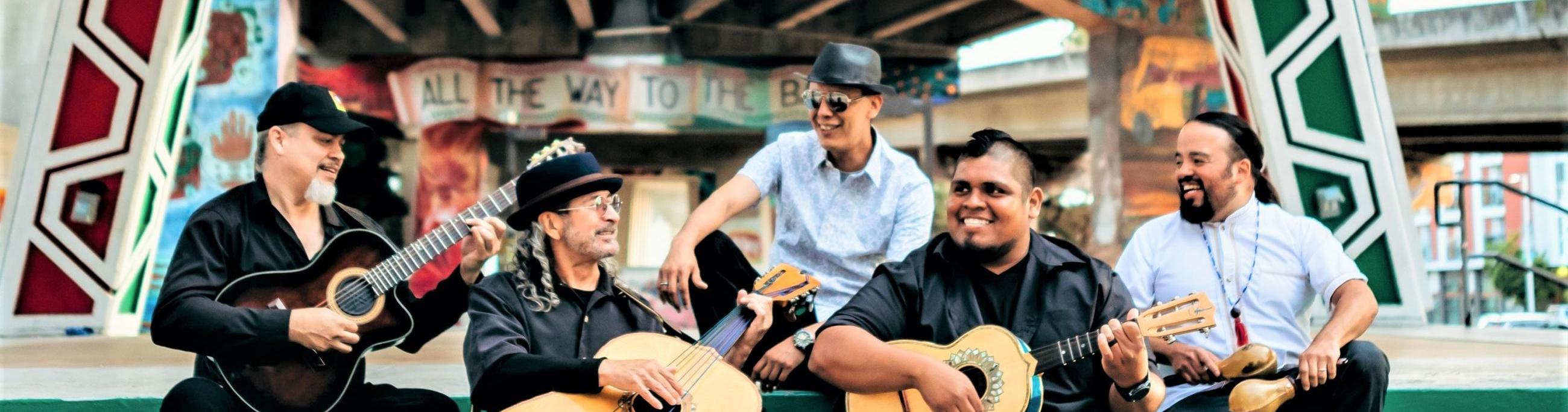 five men with instruments sitting on steps, smiling and looking at each other