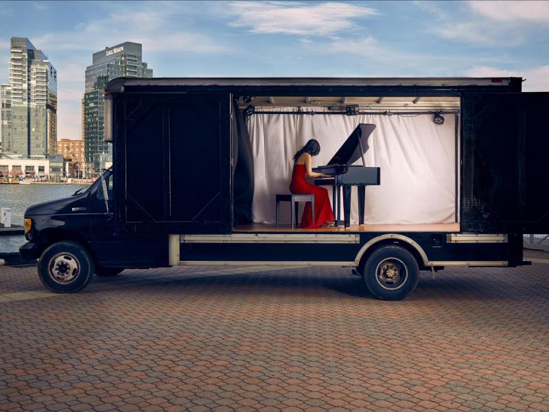 pianist in red dress playing piano inside of a truck