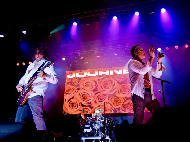 Guitarist and vocalist in foreground, drummer in background on stage