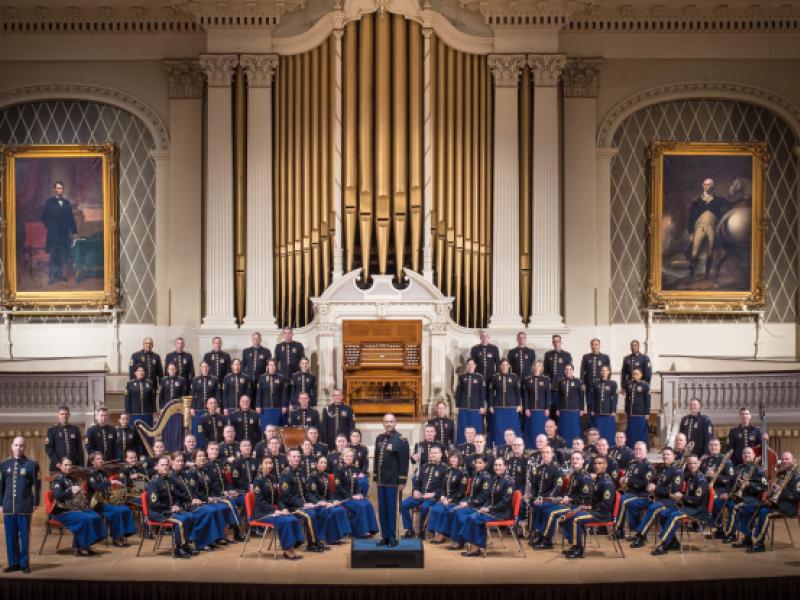 A symphony of players sits on a stage in their Army dress blues.