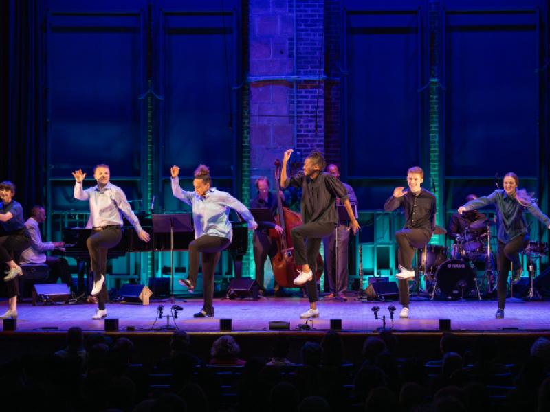 six dancers on stage smiling with right arms up and left knees raised up