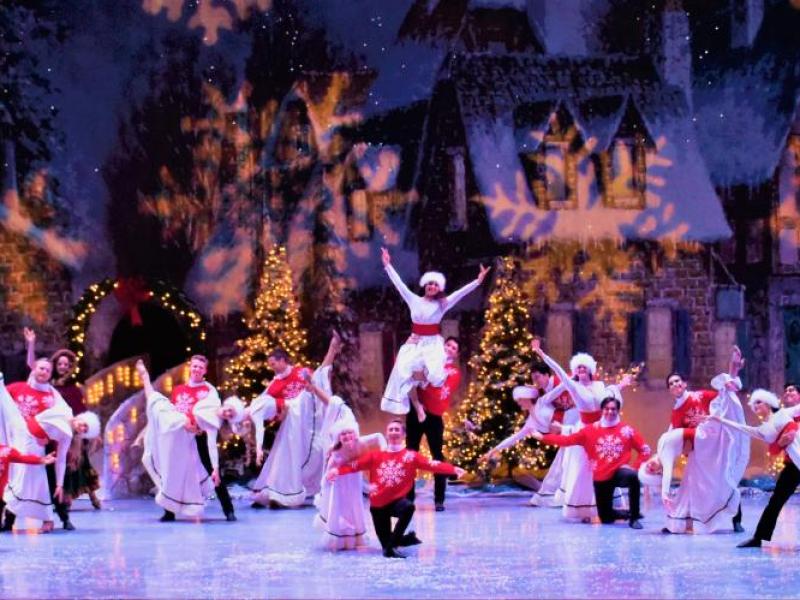 Group of dances on stage dressed in white dresses, red sweaters with snowflake shaped lighting