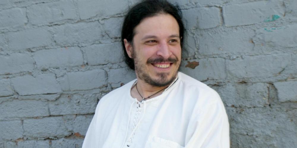 León Santiago sits in front of a brick wall, smiling.