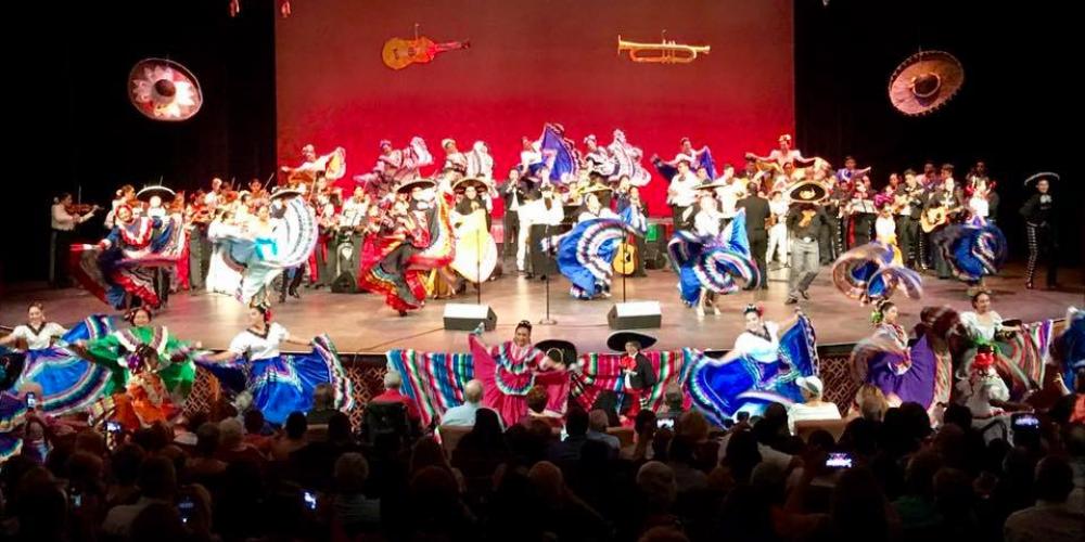 A group dressed in traditional mariachi clothing stands on the stage performing