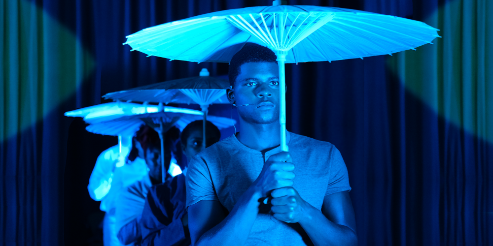 A line of people, washed in blue light, face forward and holding umbrellas over their heads