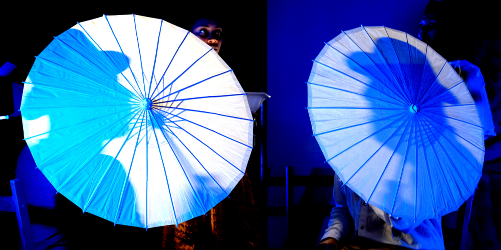 Two white umbrellas are back lit, each with the silhouette of a man wearing a bowler hat 