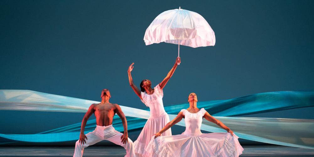 three dancers dressed in white while the dancer in the middle holds a umbrella 