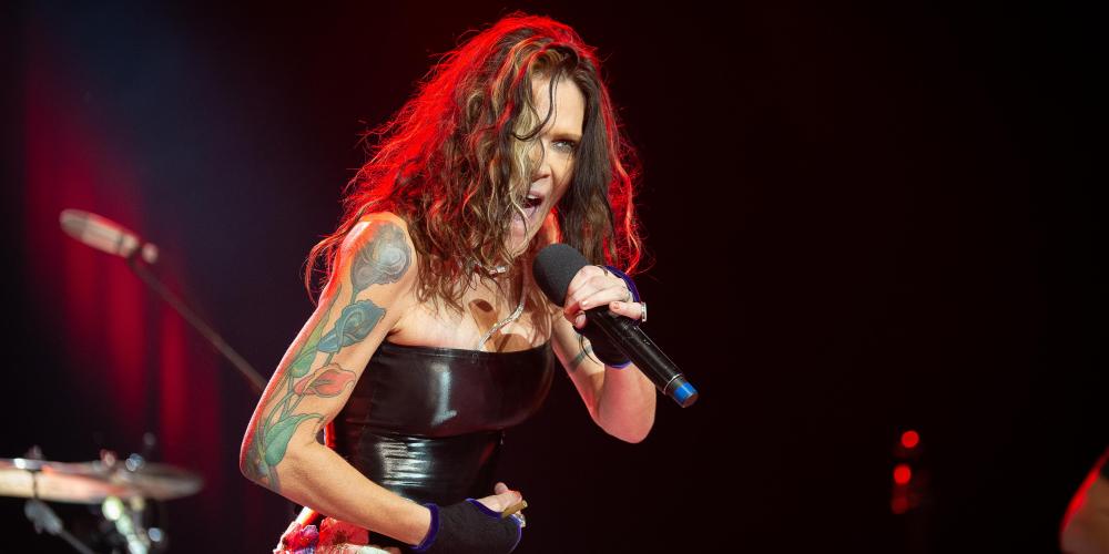 woman with long brown hair wearing a tight black strapless top singing into a microphone