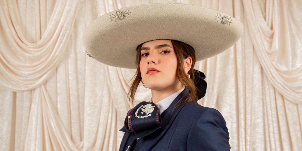 Woman posing in navy blue traje de charro outfit with a cream colored hat