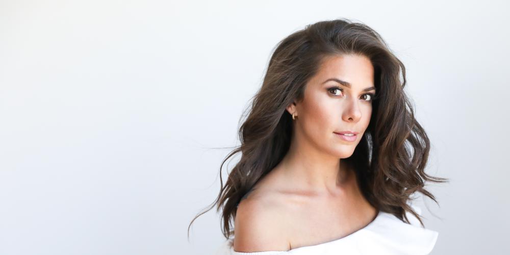 Caro Pierotto dressed in a white dress, her brown hair flowing over one shoulder