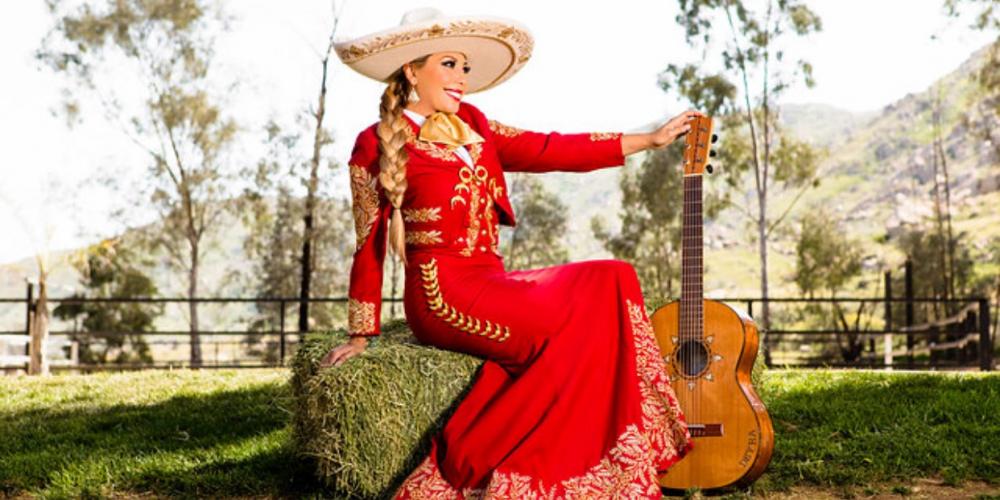 Deyra Berrera sits on a boulder wearing a red mariachi dress suit and large sombrero