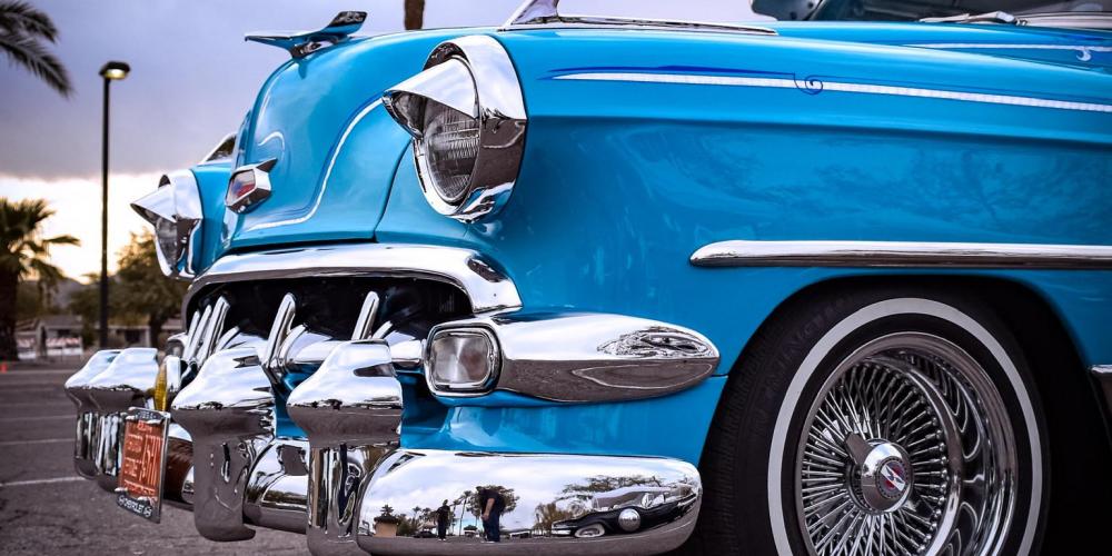 The photo shows a vintage blue car with a chrome bumper and white wall tires