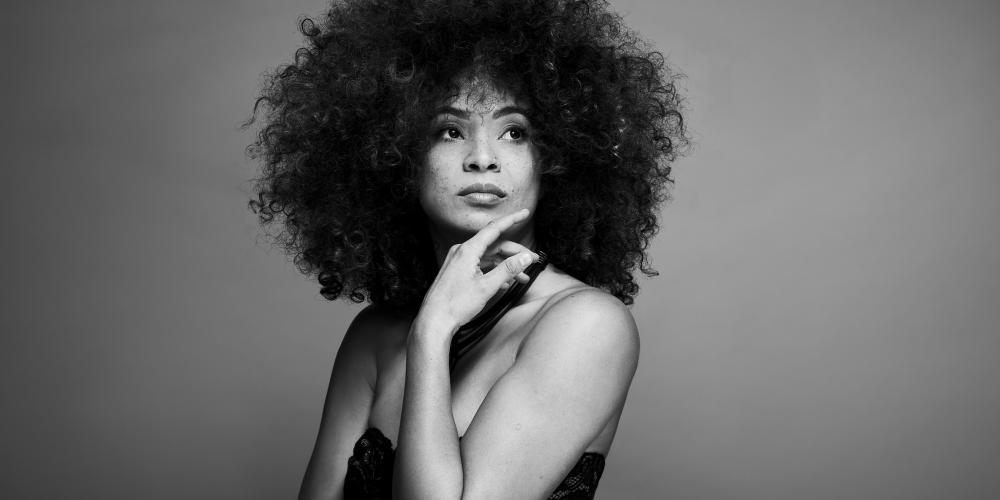 Kandace Springs poses with her hand under her chin, wearing a black dress