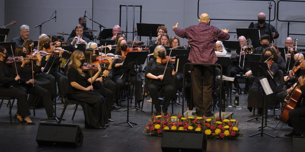 An orchestra plays on a stage with the conductor in front of them. 