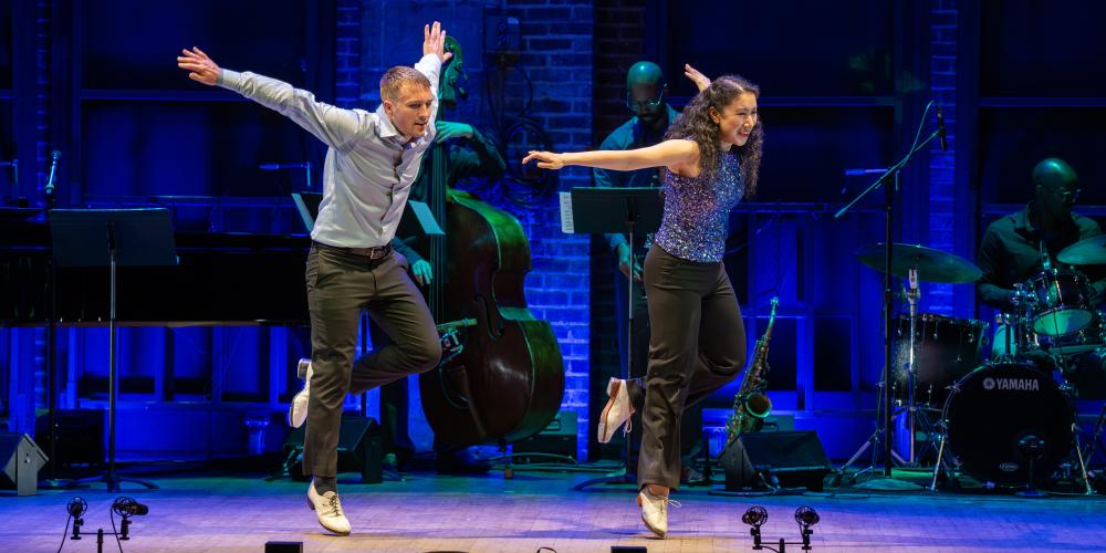 two dancers on stage with both arms outstretched behind them and left legs kicked up behind them