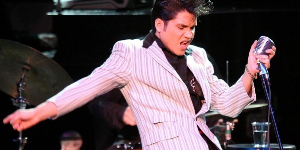 Man in a striped white suit and black pants swaying his hips to the side while holding a microphone
