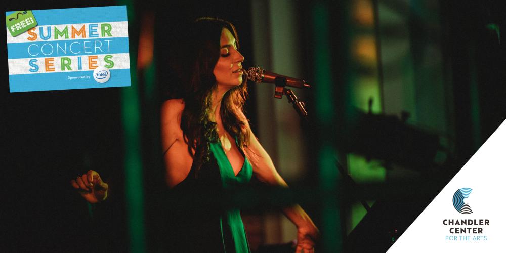 A woman wears a kelly green dress, eyes closed as she sings into a micorphone. 