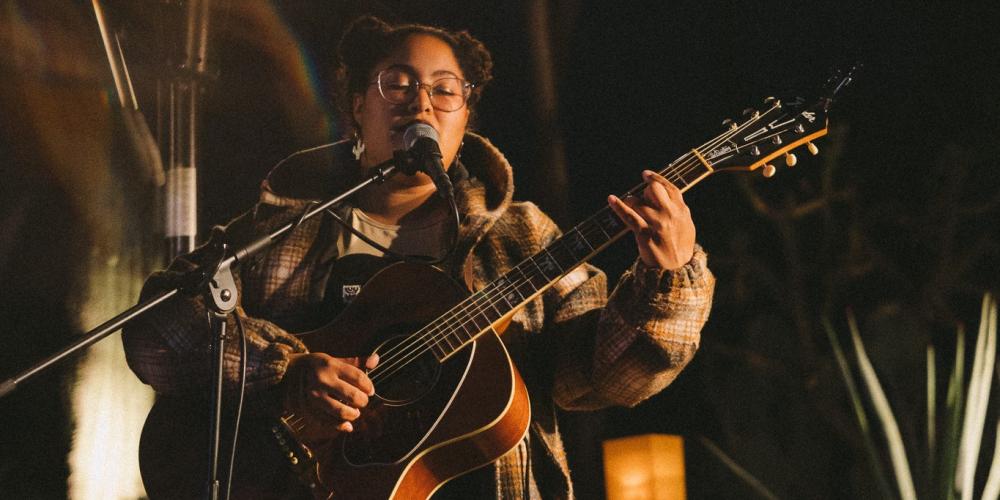 Person playing acoustic guitar and singing into a mic in an outdoor setting