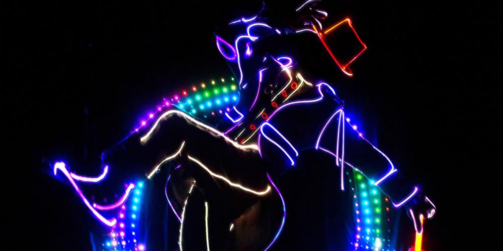 iLuminate performer on a dark stage lit and outlined as man with a top hat, suit and cane