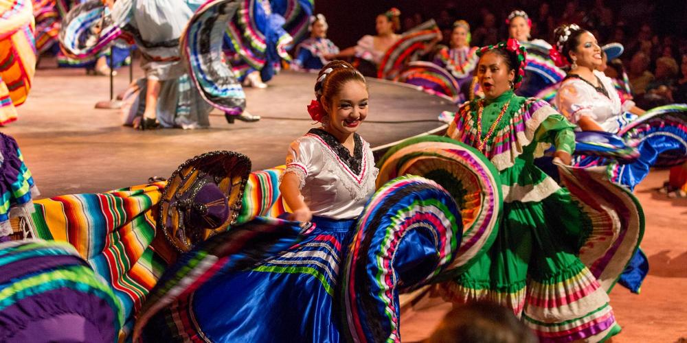 Brightly dressed dancers flourish their traditional Mexican dance skirts in front of a stage