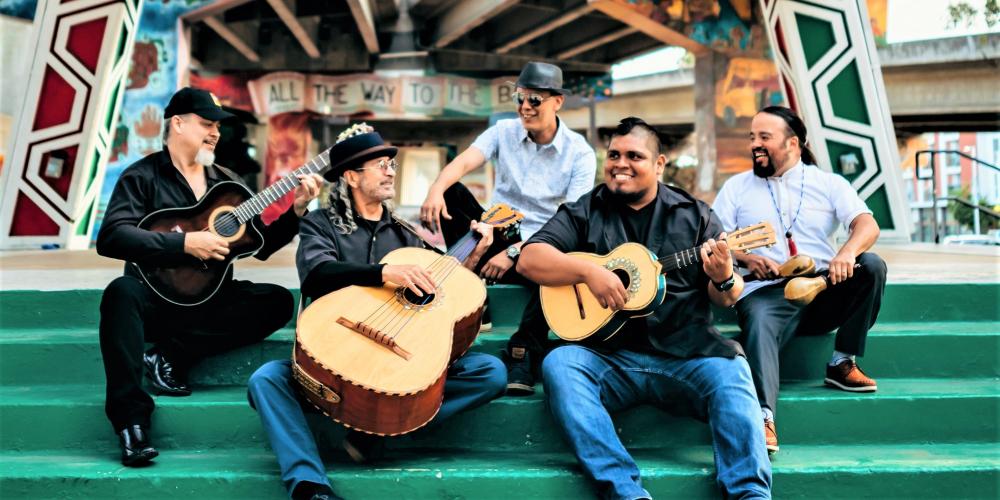 Five men sit on green stairs, some of them holding string instruments.