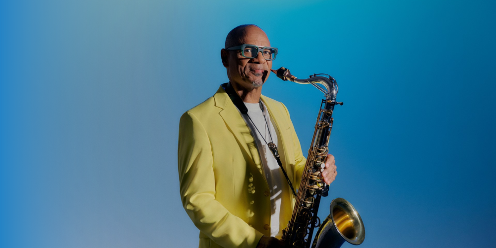 African American man wearing a yellow blazer holding a saxophone.