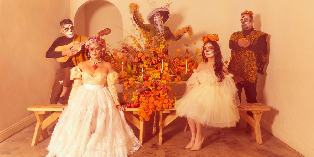 Five people pose, dressed in costumes and faces painted skeletons