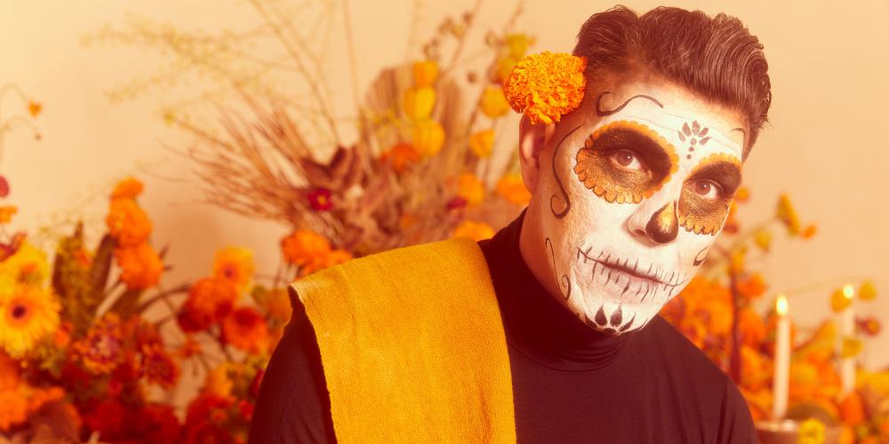 A man with dark hair and a face painted like a skeleton looks at the camera