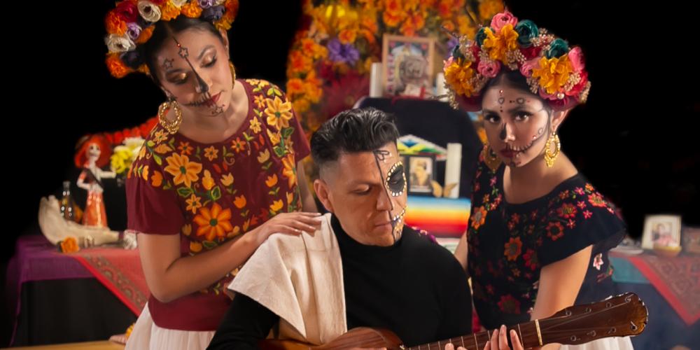 Three people pose with their faces painted with skeletons - two women and a man playing guitar