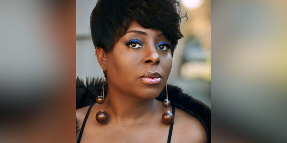 Close headshot of woman with short hair, blue eyeshadow, long earrings and black cover