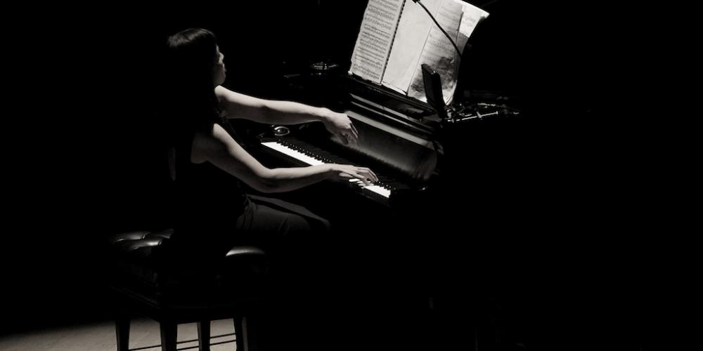 a woman playing the piano in a shadowy room