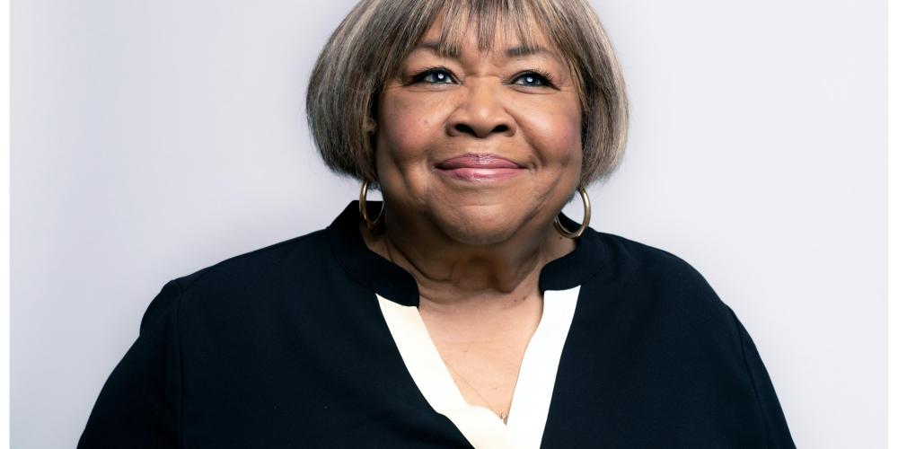 Mavis Staples smiling headshot in front of white background, dressed in black with black earrings