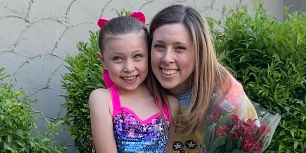 A blond woman poses with a young dancer dressed in a rainbow colored dress
