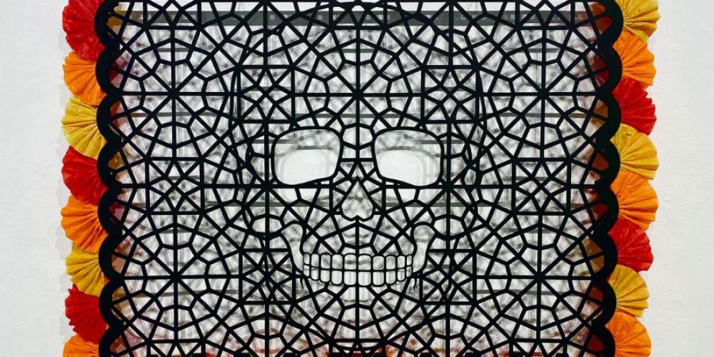 black rectangle with decorative cut outs making up a skeleton head. The black rectangle has red, yellow and orange fluffy decoration around the outside.