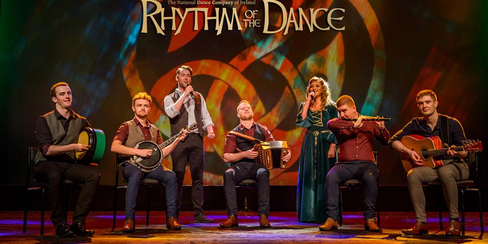 Four men hold traditional folk instruments with two singers - a woman and a man in their midst