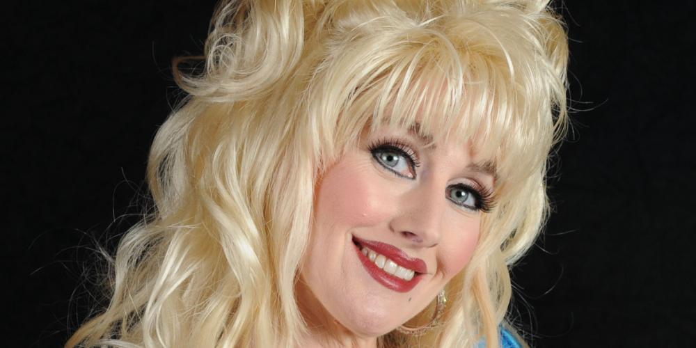 A woman in a blue dress and blond hair smiles at the camera
