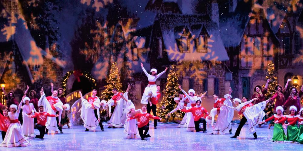 Performers dressed in white and red posing and smiling on stage in front of a glowing snowflake scene