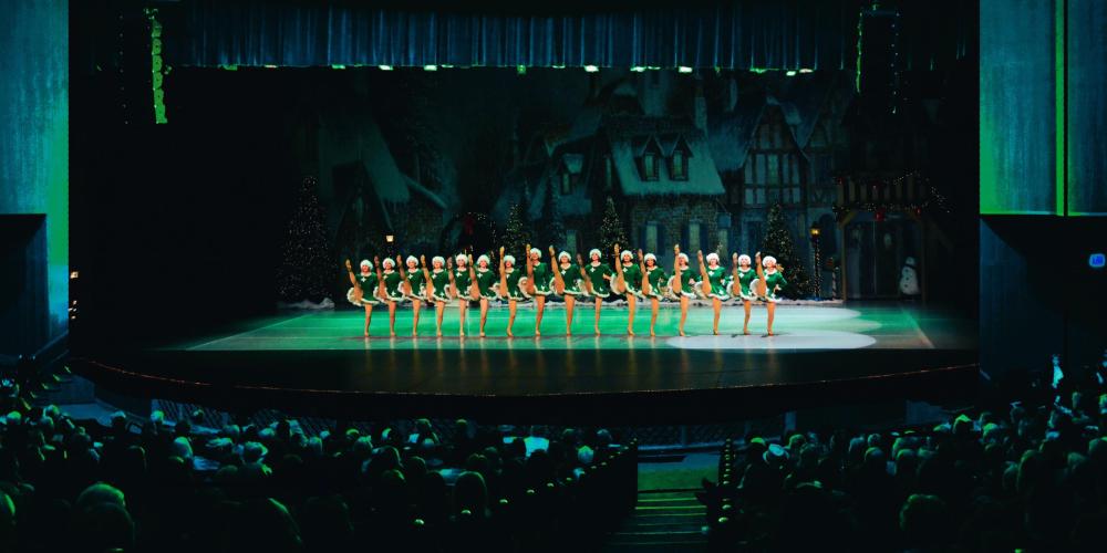 green lit stage with spirit of christmas dancers