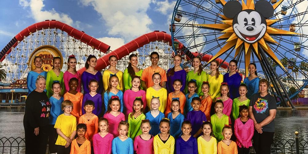 Tempe Dance students dressed in different primary color t-shirts posed in front of Disney roller coaster