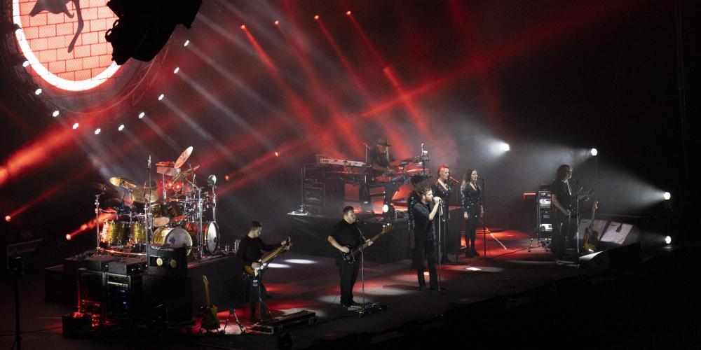 A band stands on a stage with red laser lights and an LED screen projecting a kangaroo