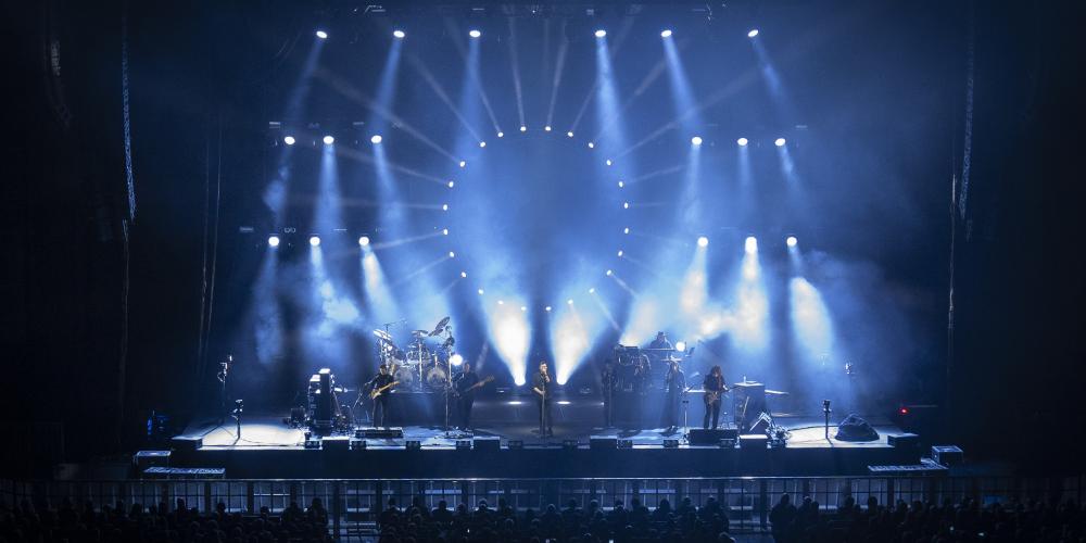 A band performs on a stage with dramatic blue lights streaming around them