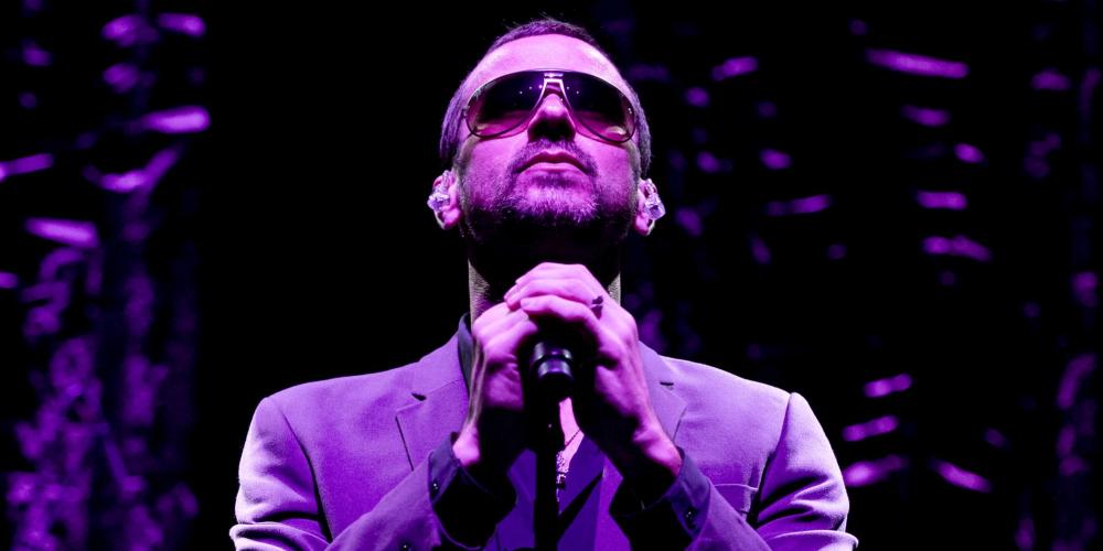 On stage wearing a purple jacket and wearing sunglasses