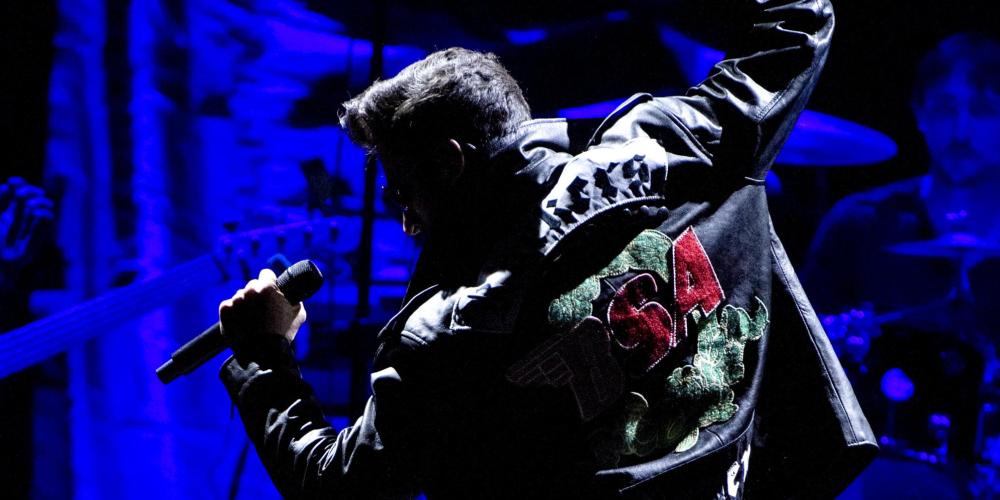 Performing on stage with black leather jacket with red rose on back