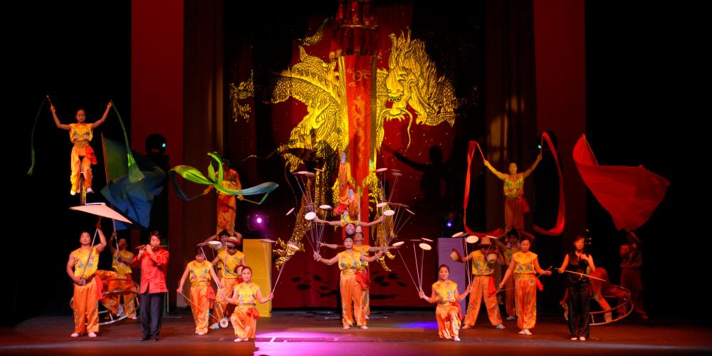 The Peking Acrobats on stage with colorful red and yellow costumes spinning plates