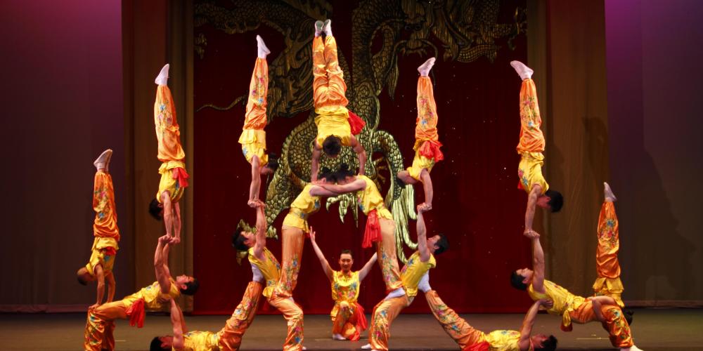 The Peking Acrobats on stage creating a human pyramid dressed in colorful red and orange costumes