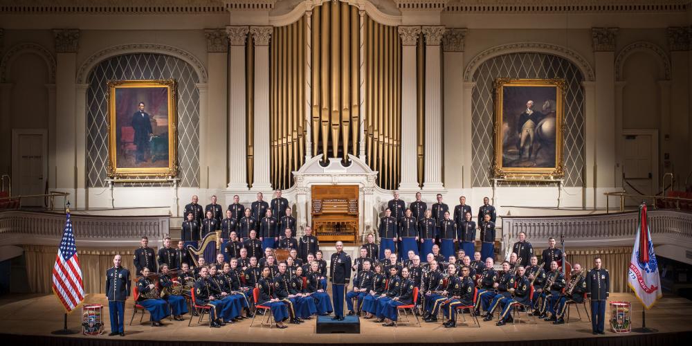 A symphony of players sits on a stage in their Army dress blues.