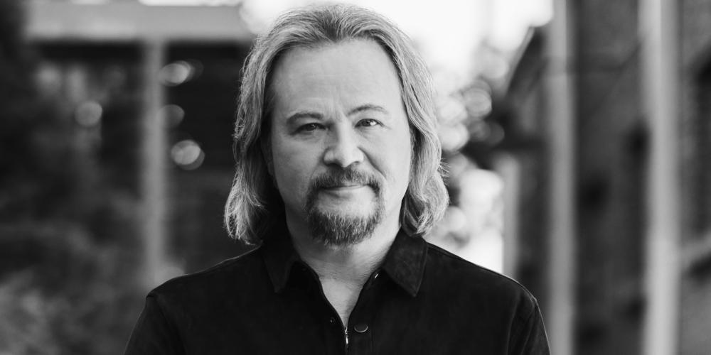 A man with shoulder-length blond hair wears a black cowboy style shirt in a black and white photo