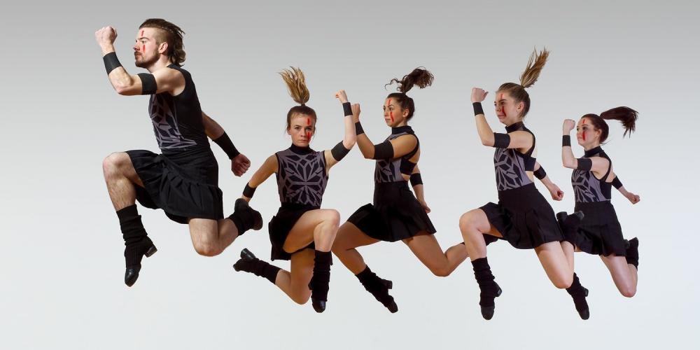 Five Members, one male and four females, of Trinity Irish Dance Company leaping forward through the air