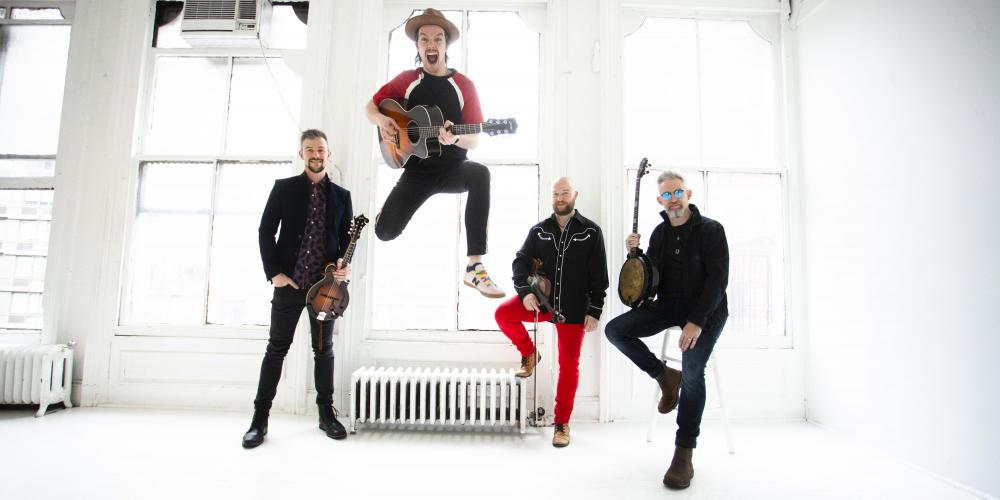 We Banjo 3 in a white room with their instruments; lead singer jumping in the air